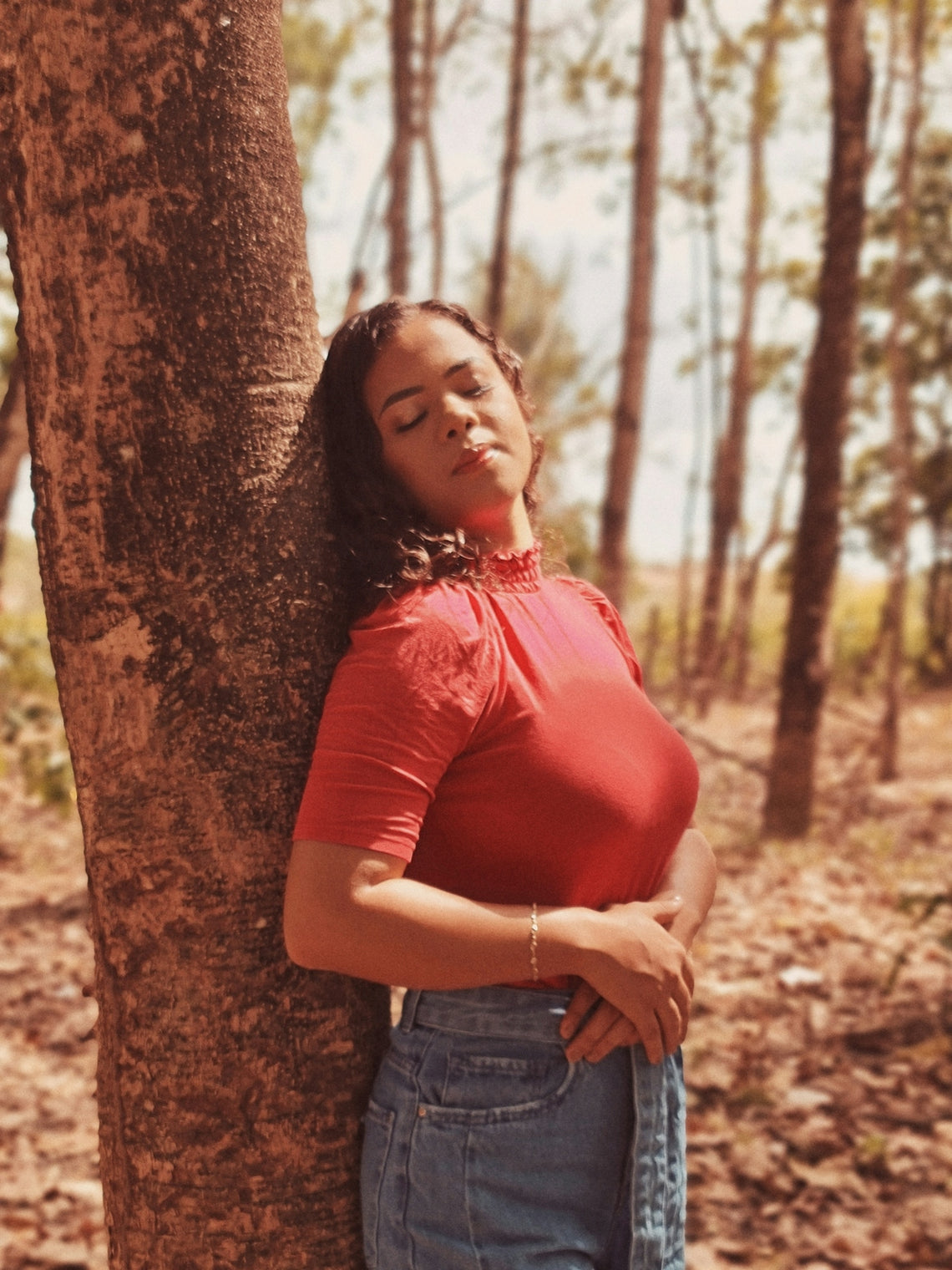 woman in red shirt and blue denim shorts leaning on brown tree