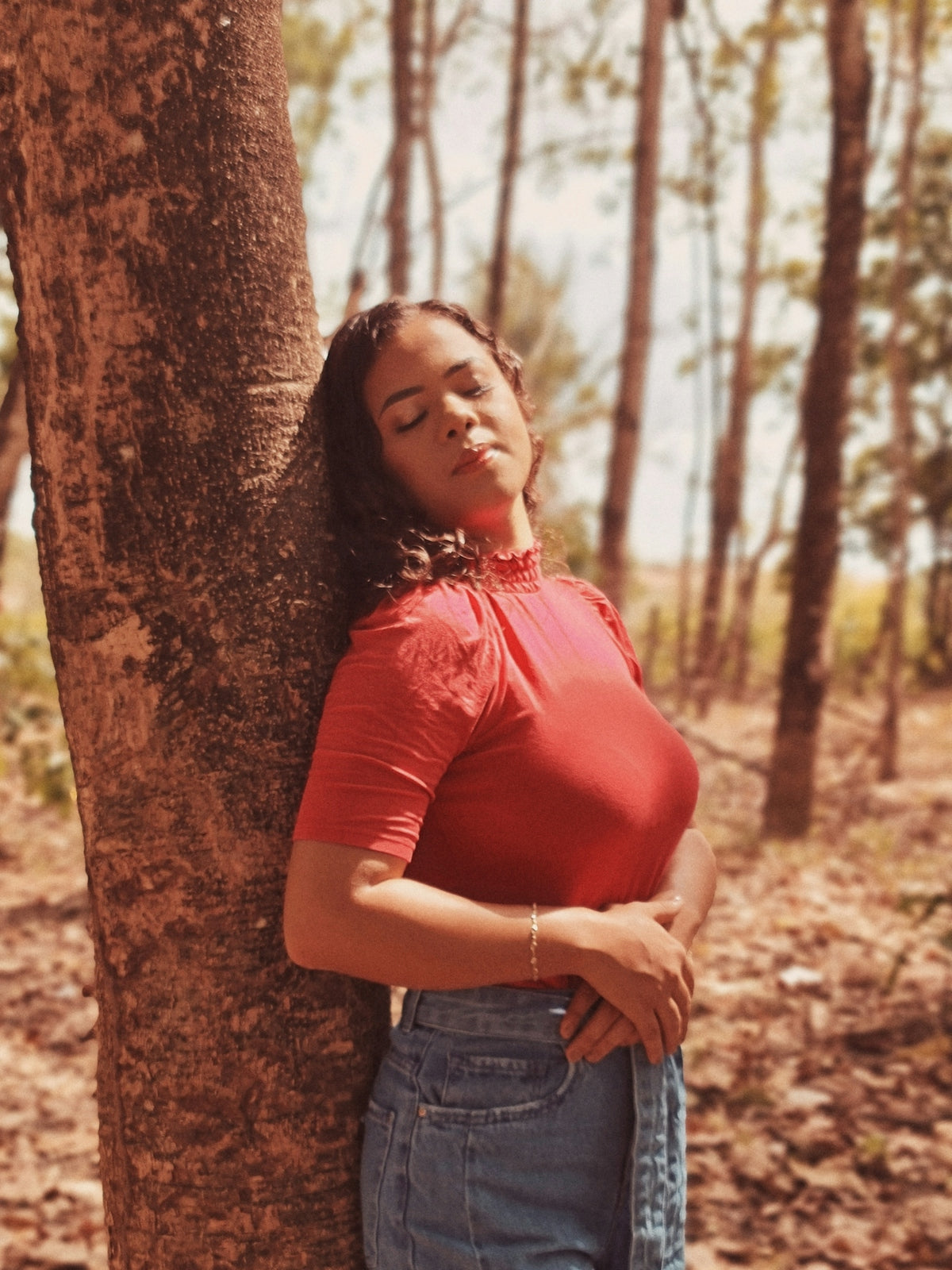 woman in red shirt and blue denim shorts leaning on brown tree