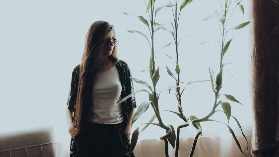 a woman standing in front of a window next to a plant