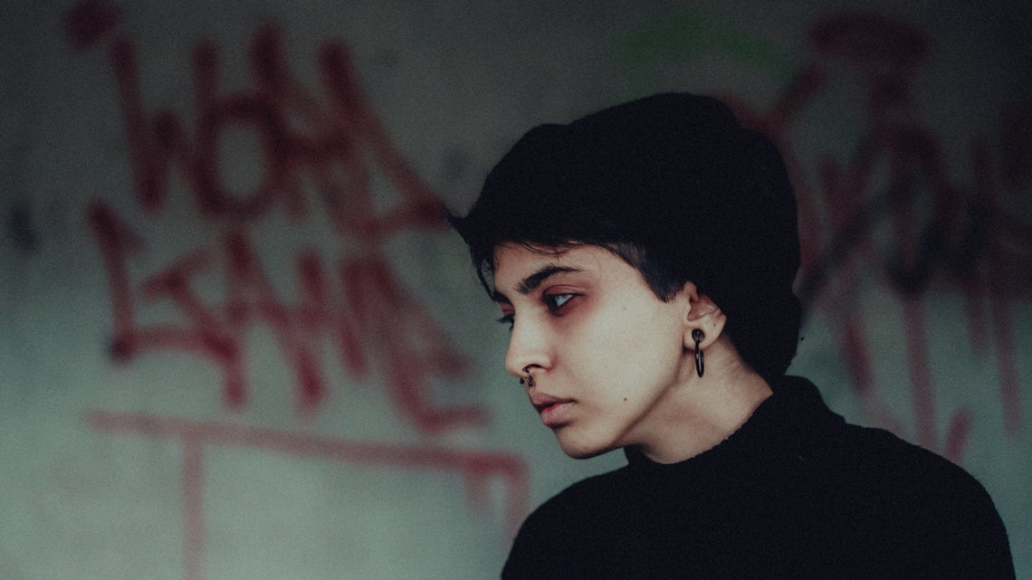 a young man with ear piercings standing in front of a graffiti covered wall