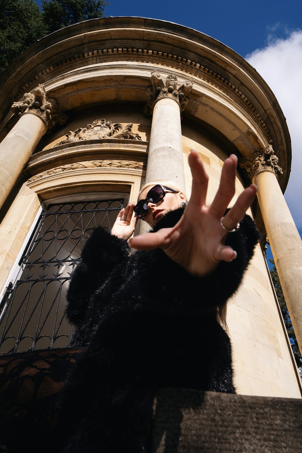 Woman in sunglasses reaches out near building.
