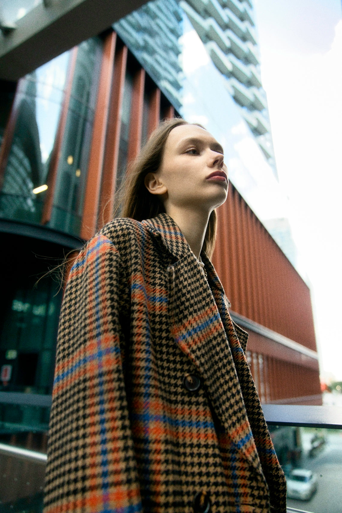 Young woman in plaid coat near modern building