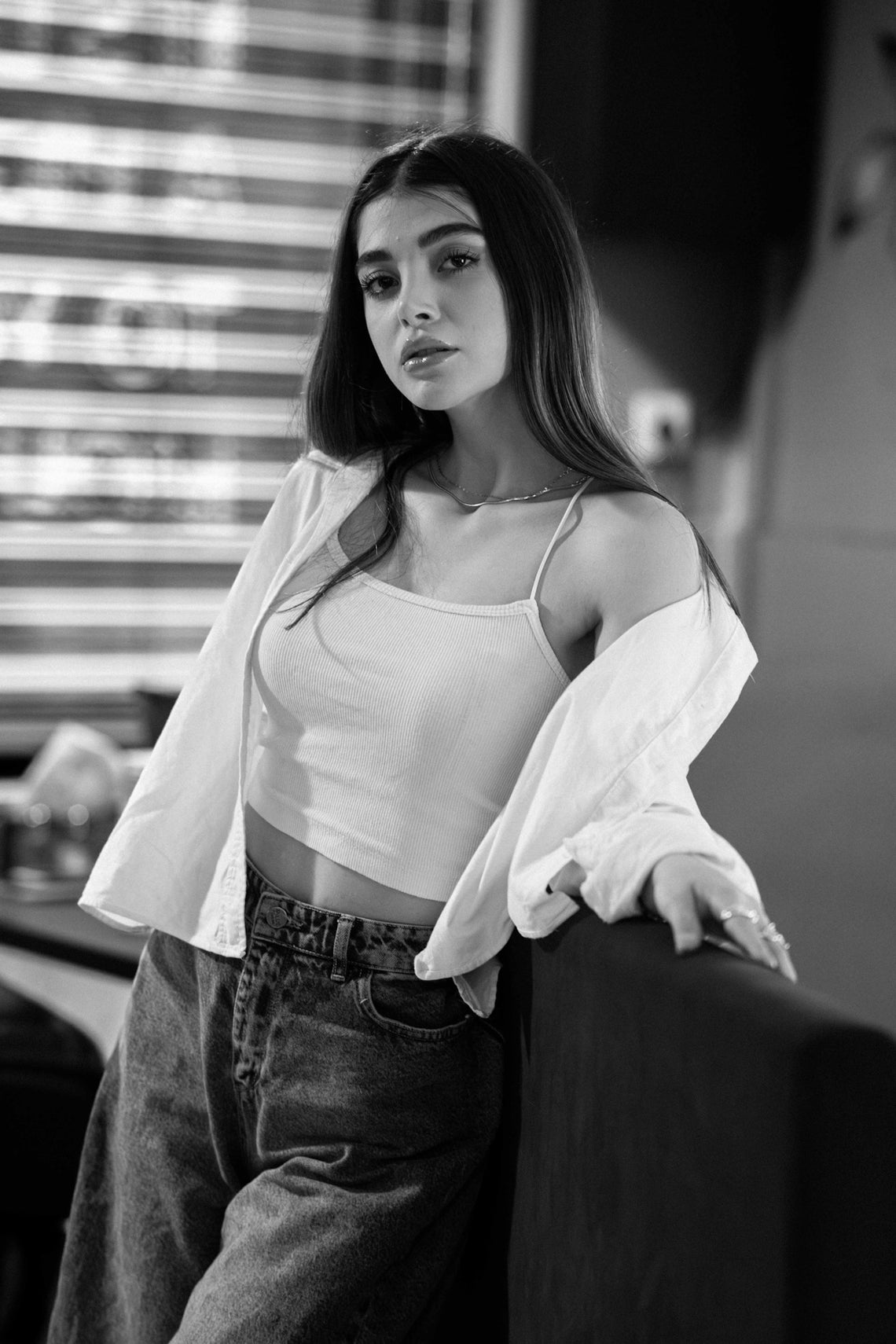 A young woman in casual clothing leans on furniture.