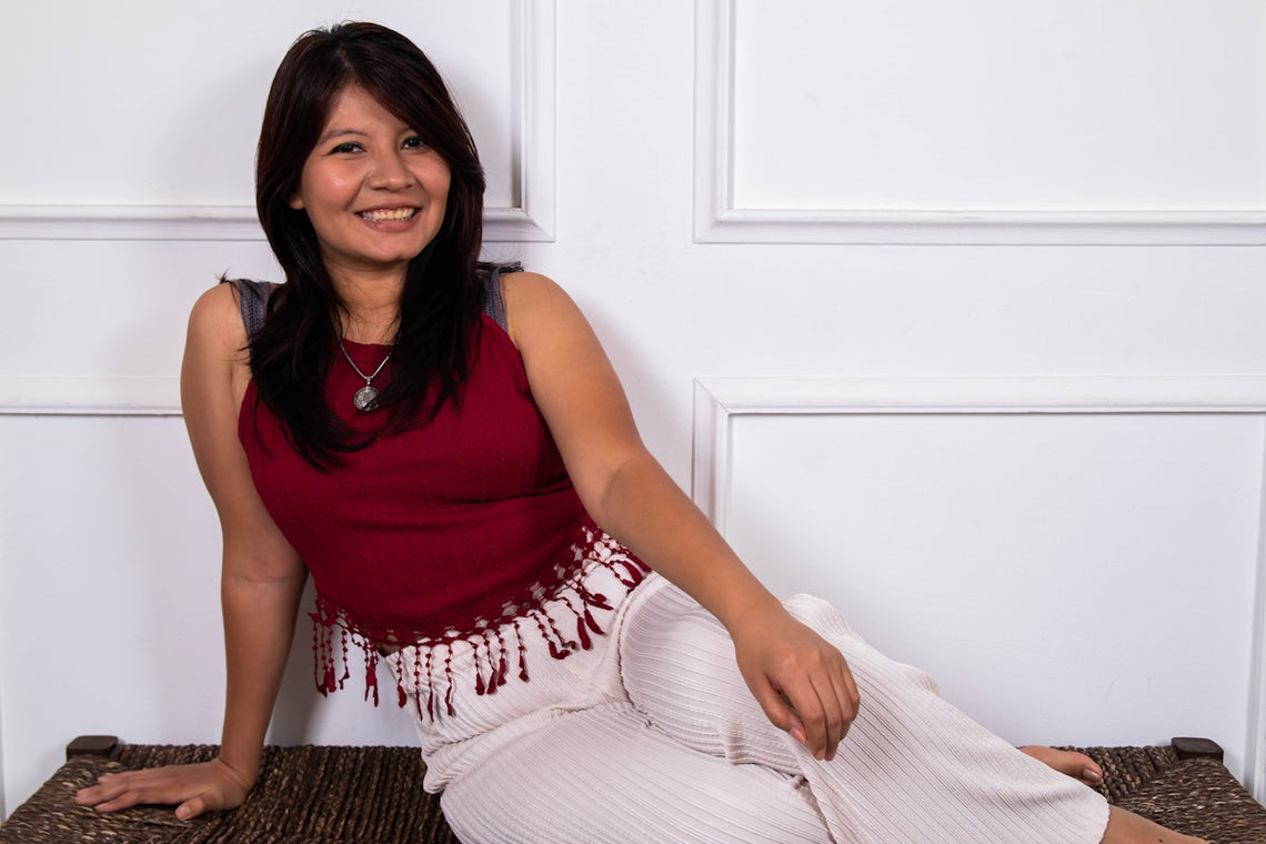 A smiling woman in casual clothing sits on a bench.