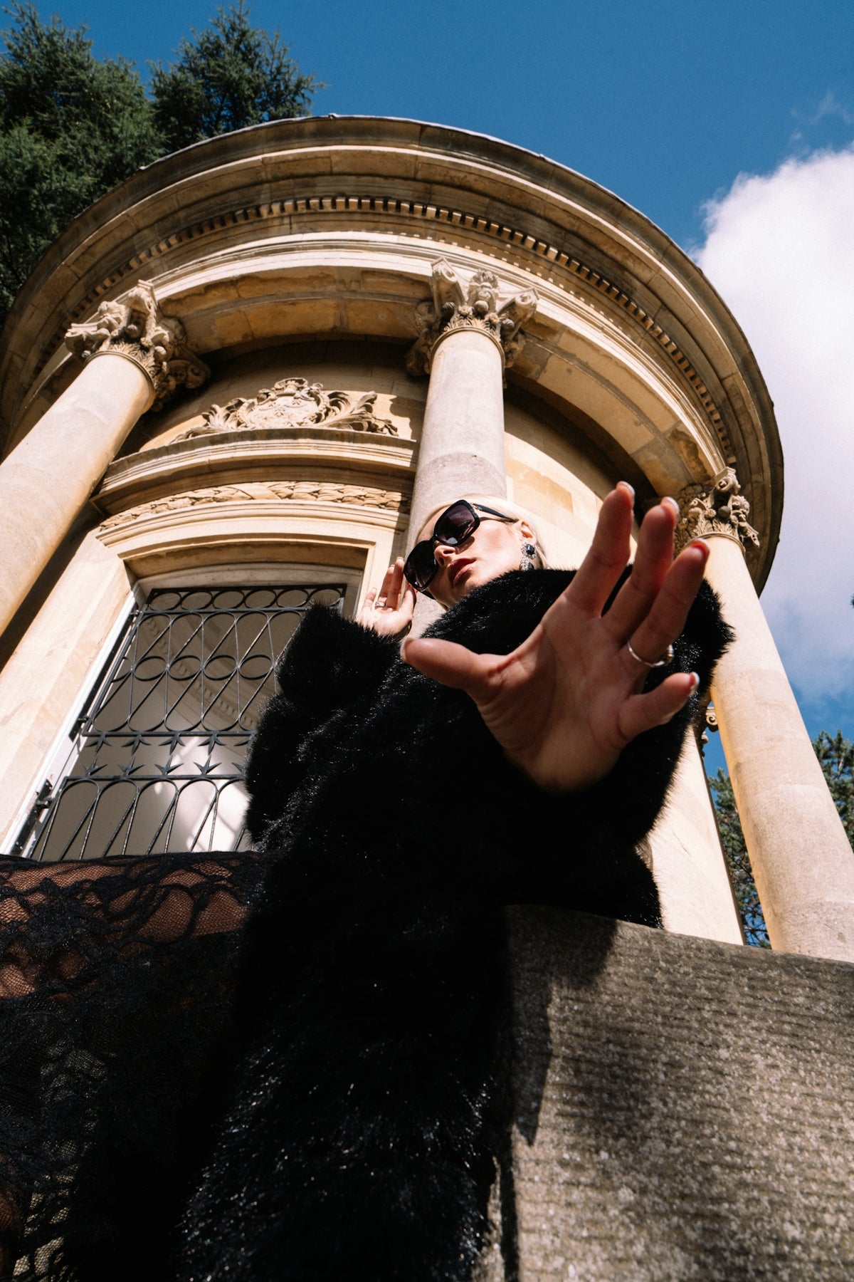Woman in black coat reaching out near old building