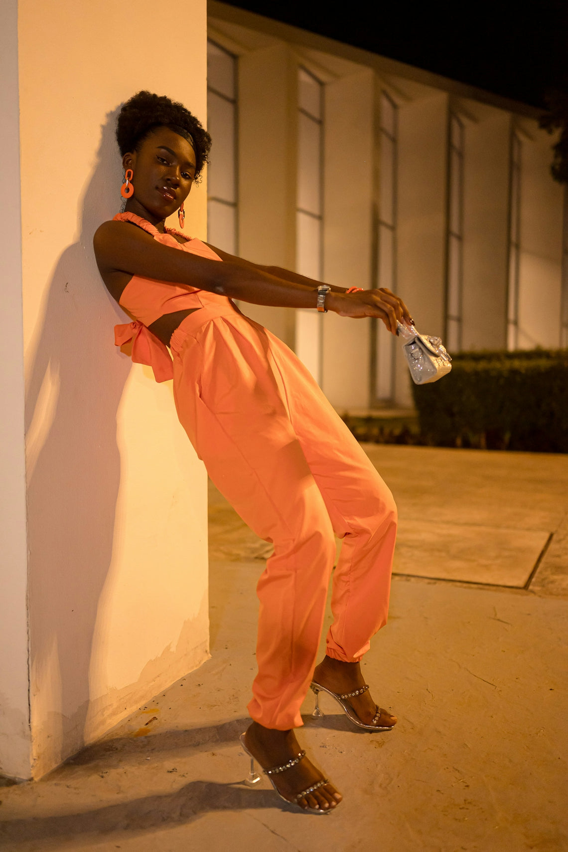 Woman in orange jumpsuit posing by wall at night