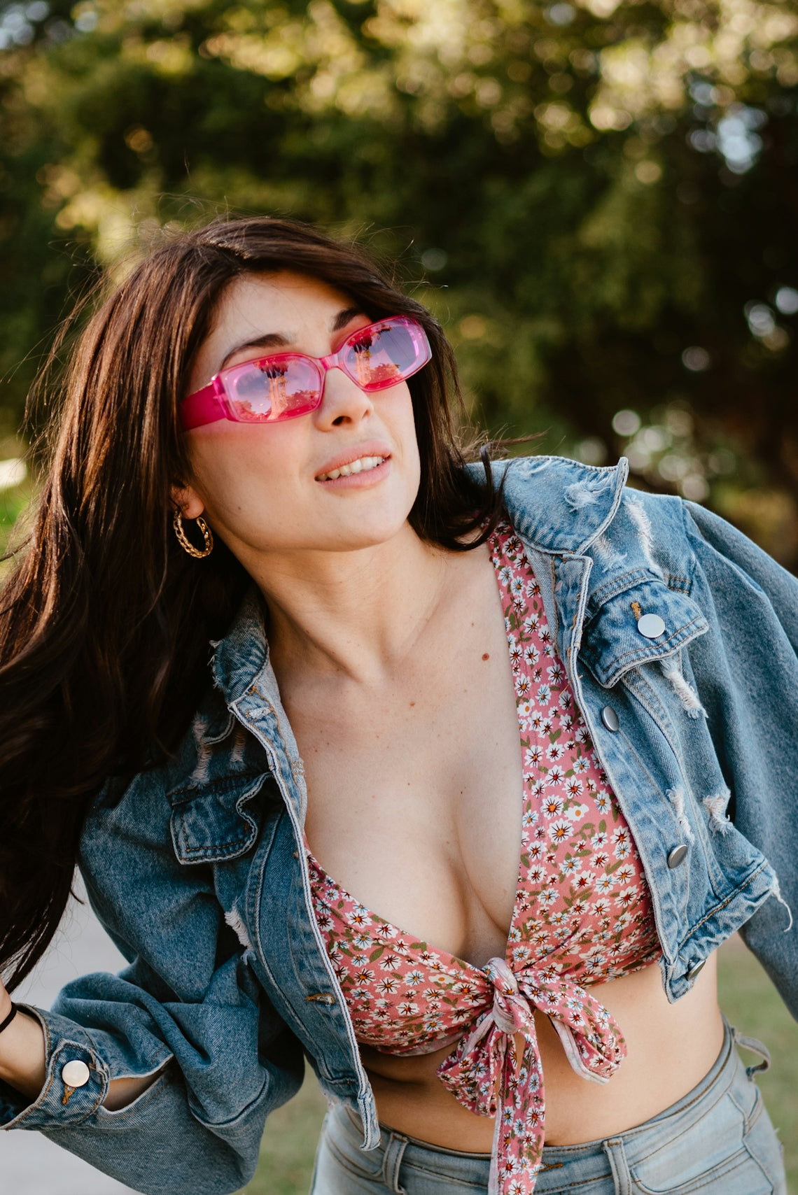 Woman in denim jacket and floral top wearing pink sunglasses