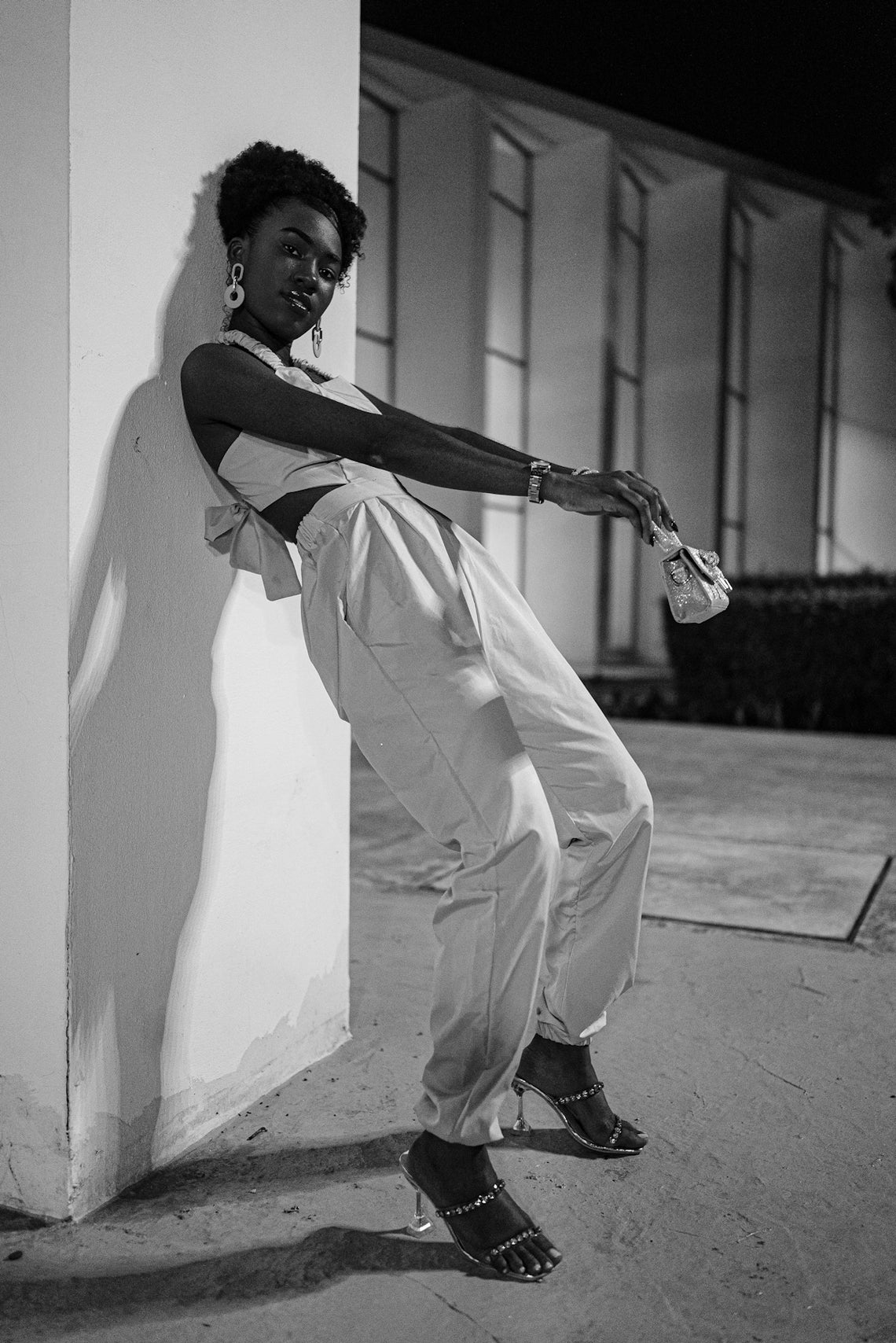 A woman in stylish clothing leans against a wall.