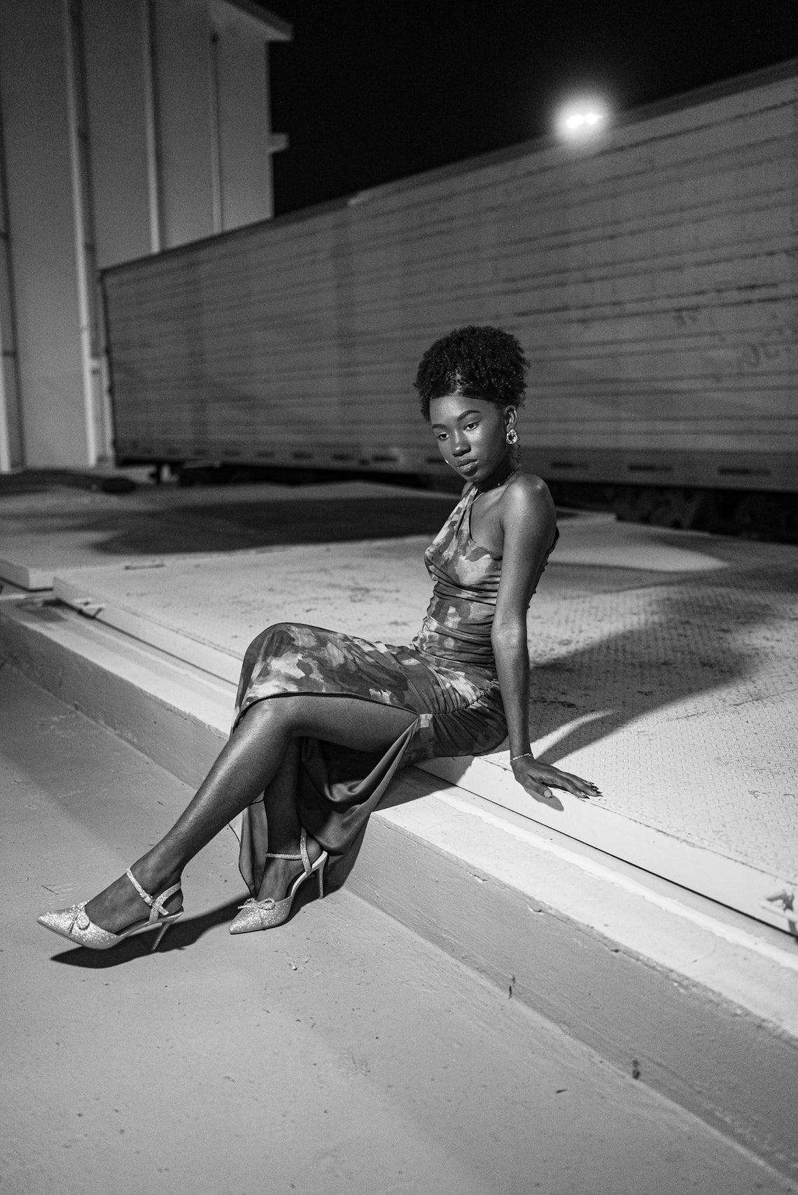Woman in a dress sitting by a curb at night.