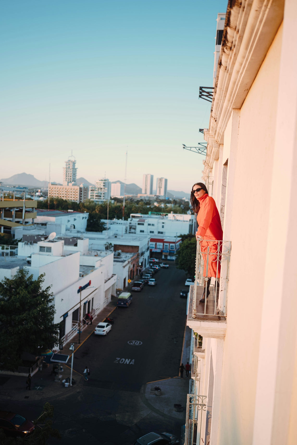 Woman in orange on a balcony overlooking city street