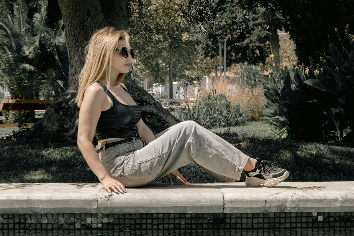 Young woman sitting on a stone ledge in a park.